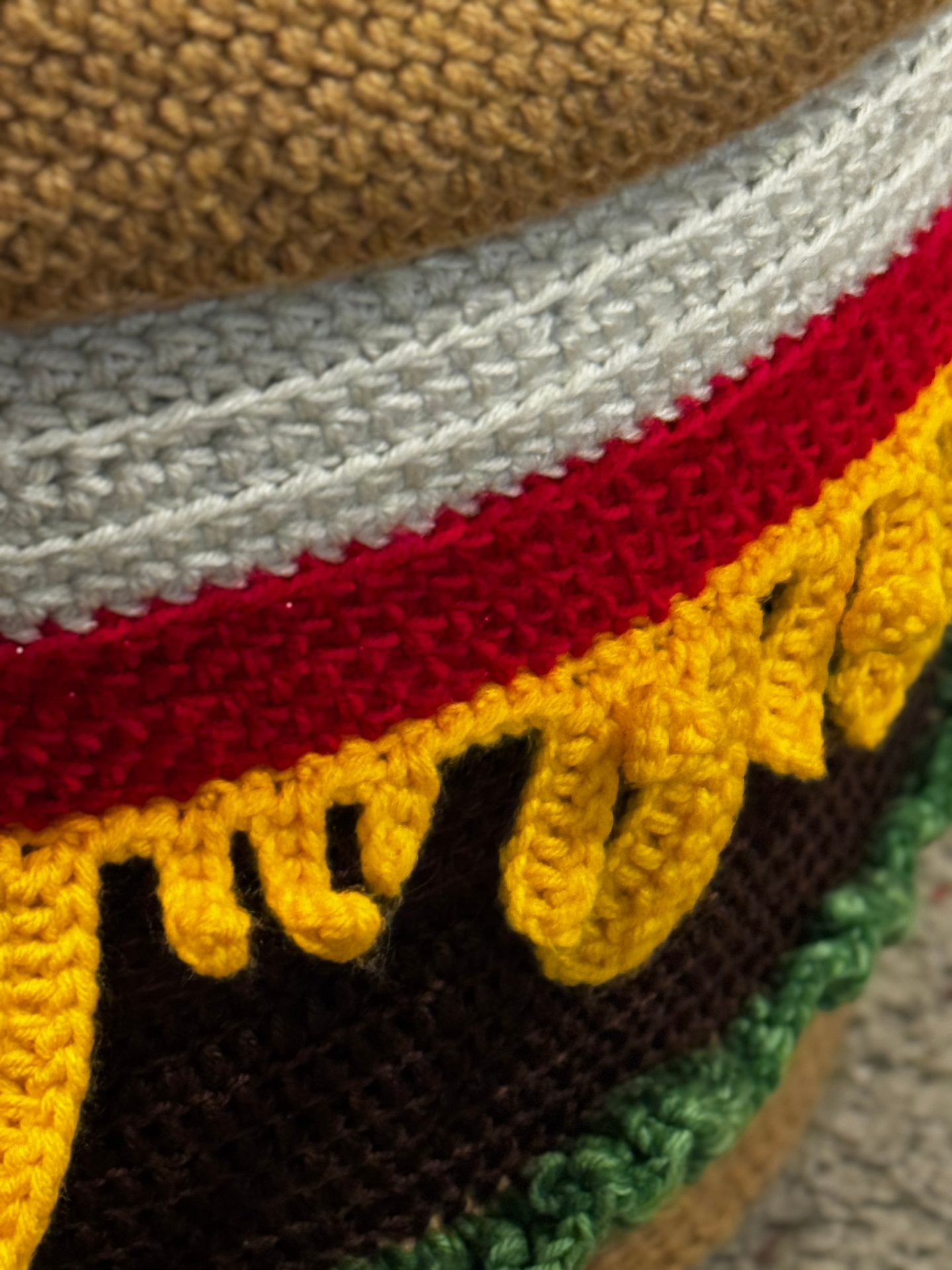 A close up of the crocheted layers showing tomato, cheese, and dripping cheese details made of many small stitches.