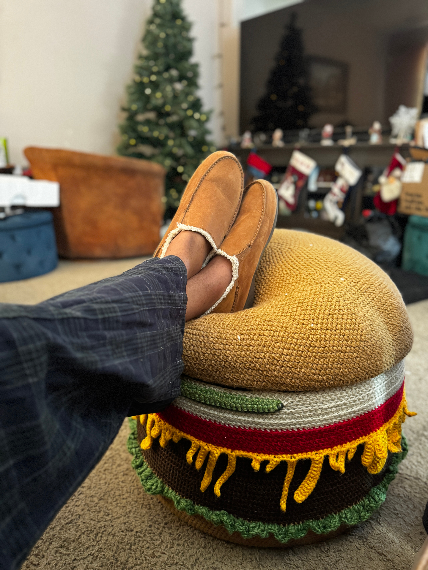 A person rests their feet on the burger ottoman in a living room.